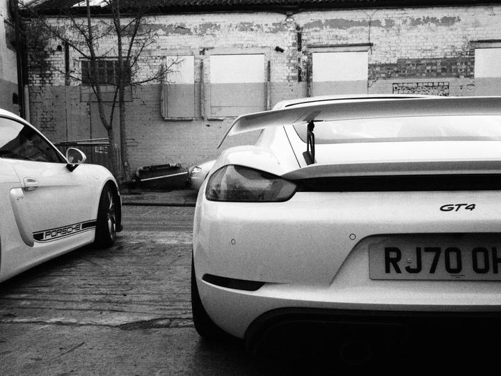 Two white Porsche 718 GT4s in the yard