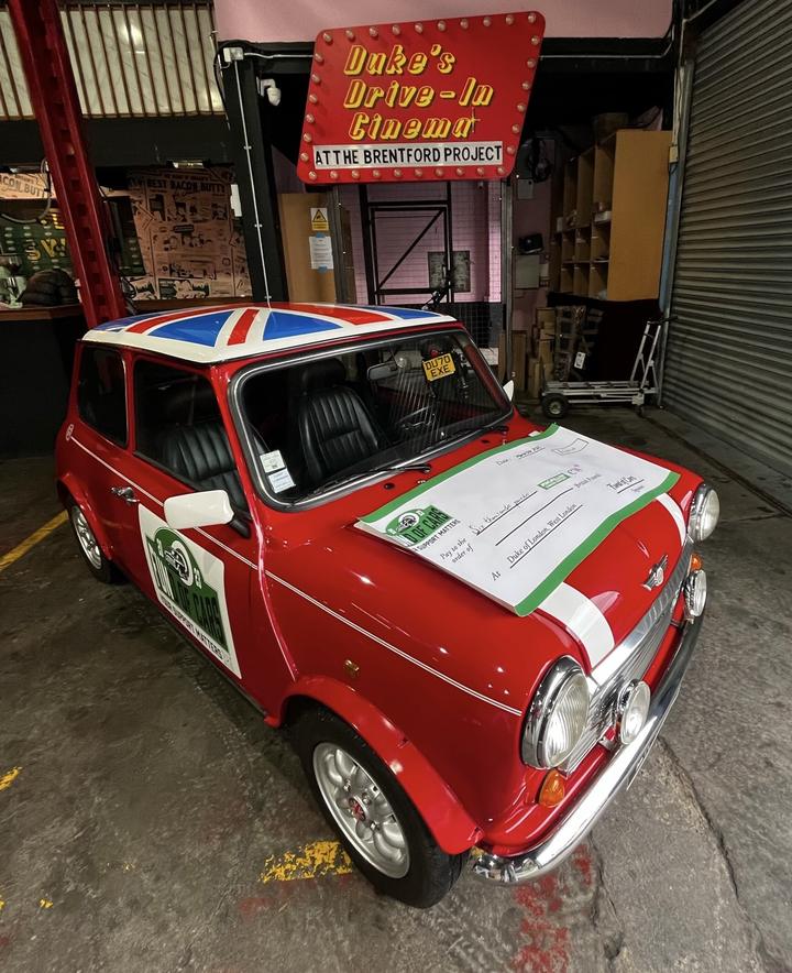 Alec's classic Mini with the giant charity cheque on the bonnet, under the Duke's Drive-In Cinema sign